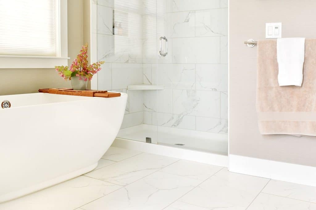 A bathroom with a white tub and shower, adorned with elegant marble-effect tiles