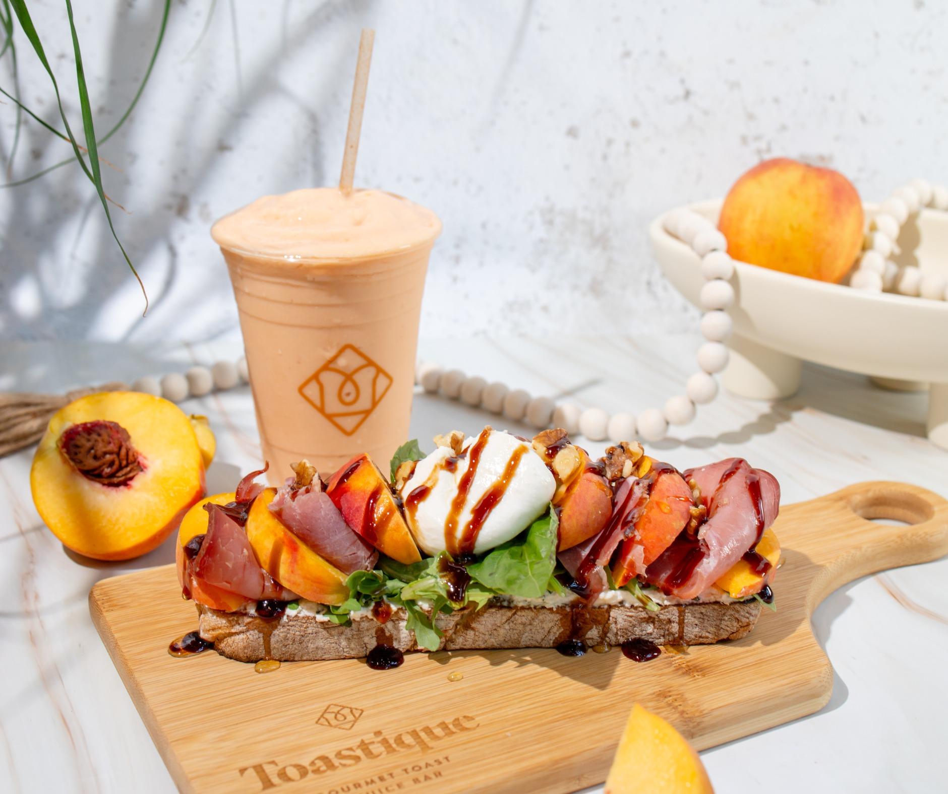 Peach & Prosciutto Toast topped with burrata, fresh peaches, and balsamic glaze served alongside a Peach Smoothie at Toastique
