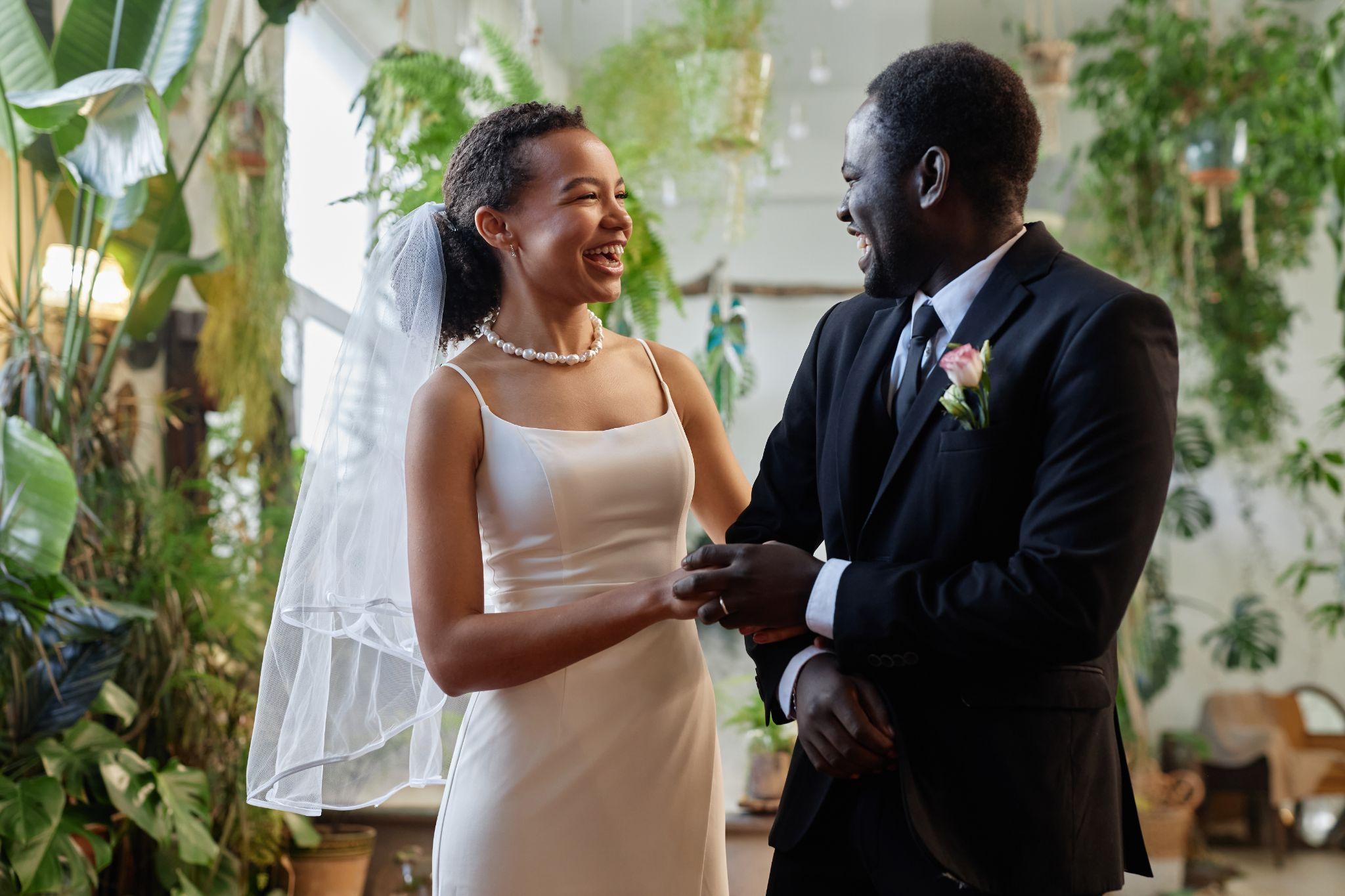 Candid bride in a satin dress and veil laughing with groom in a tropical indoor garden with natural light and greenery captured by a Sarasota wedding photographer