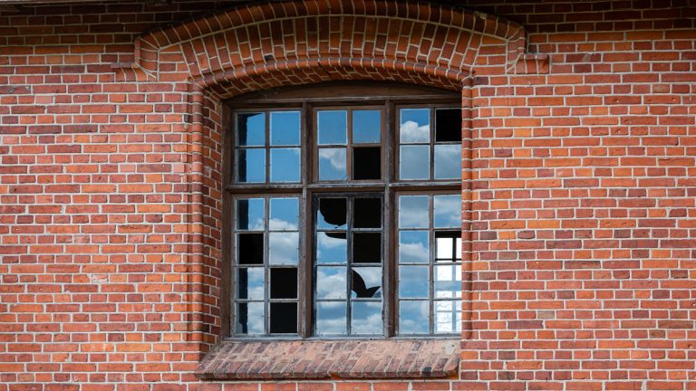 An old window with broken glass panes in a red brick wall