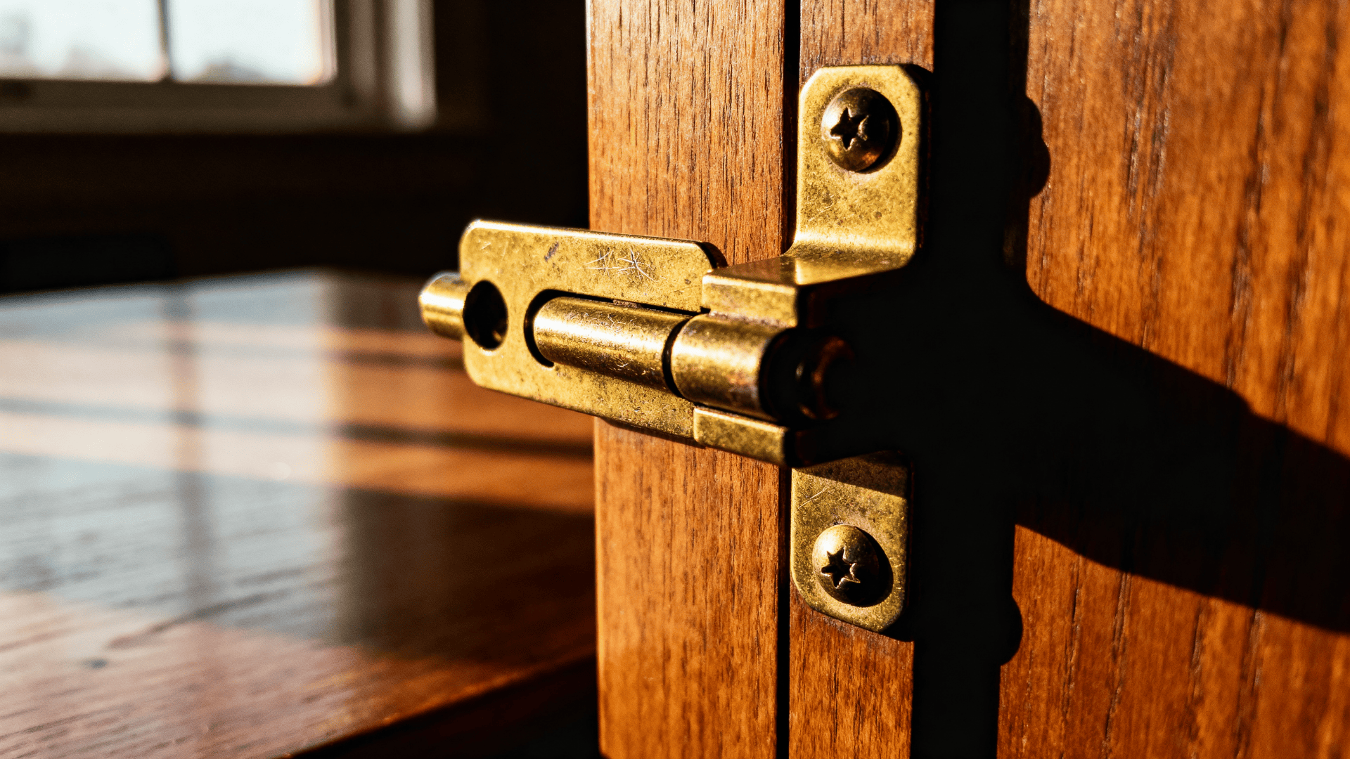 Close up of a brass drop leaf table hinge (rule joint hinge) on a wooden panel, showing the folding joint, screws, and warm light.