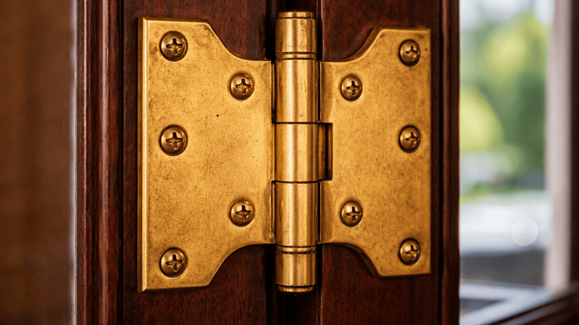 Close up of a brass parliament hinge on a wooden door, showing the cranked offset design, screws, and polished metal in warm light.