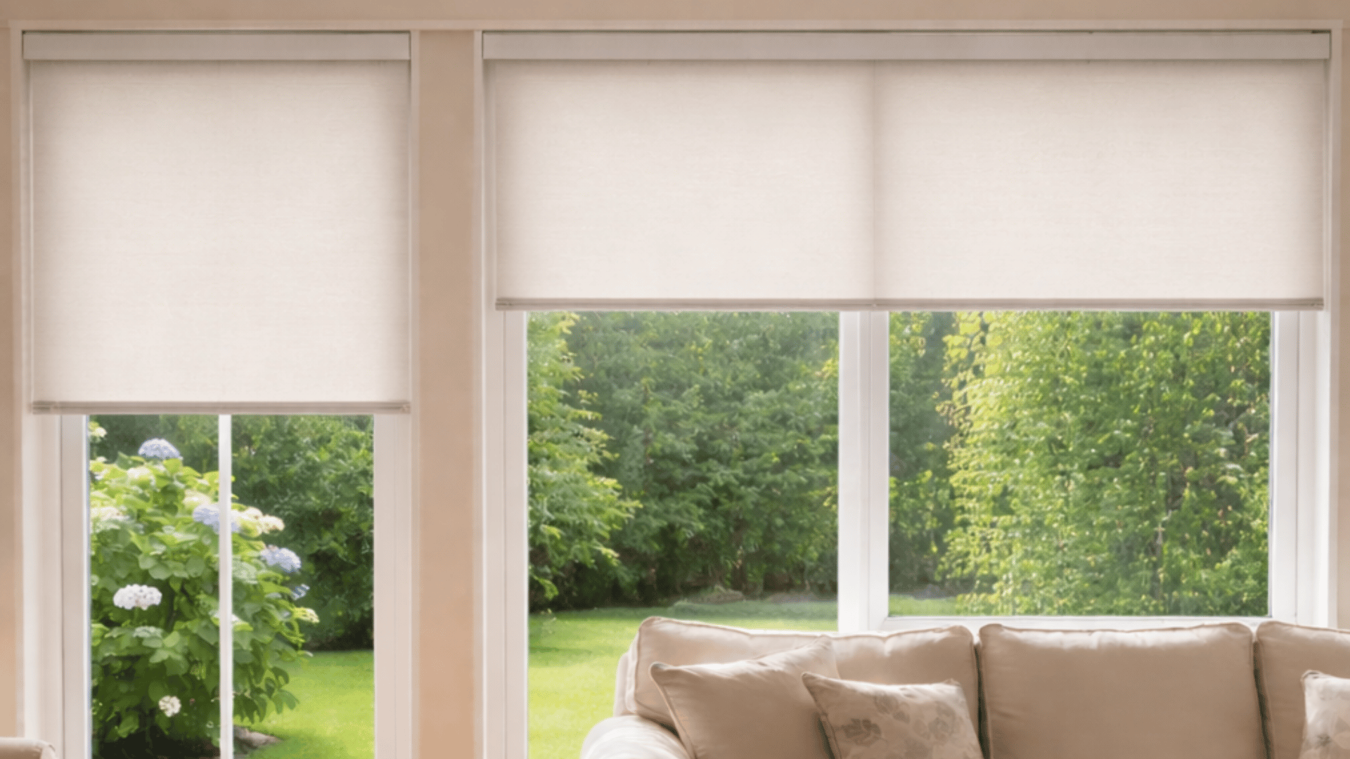a bright living room with off-white roller blinds, a beige sofa, overlooking a lush garden.