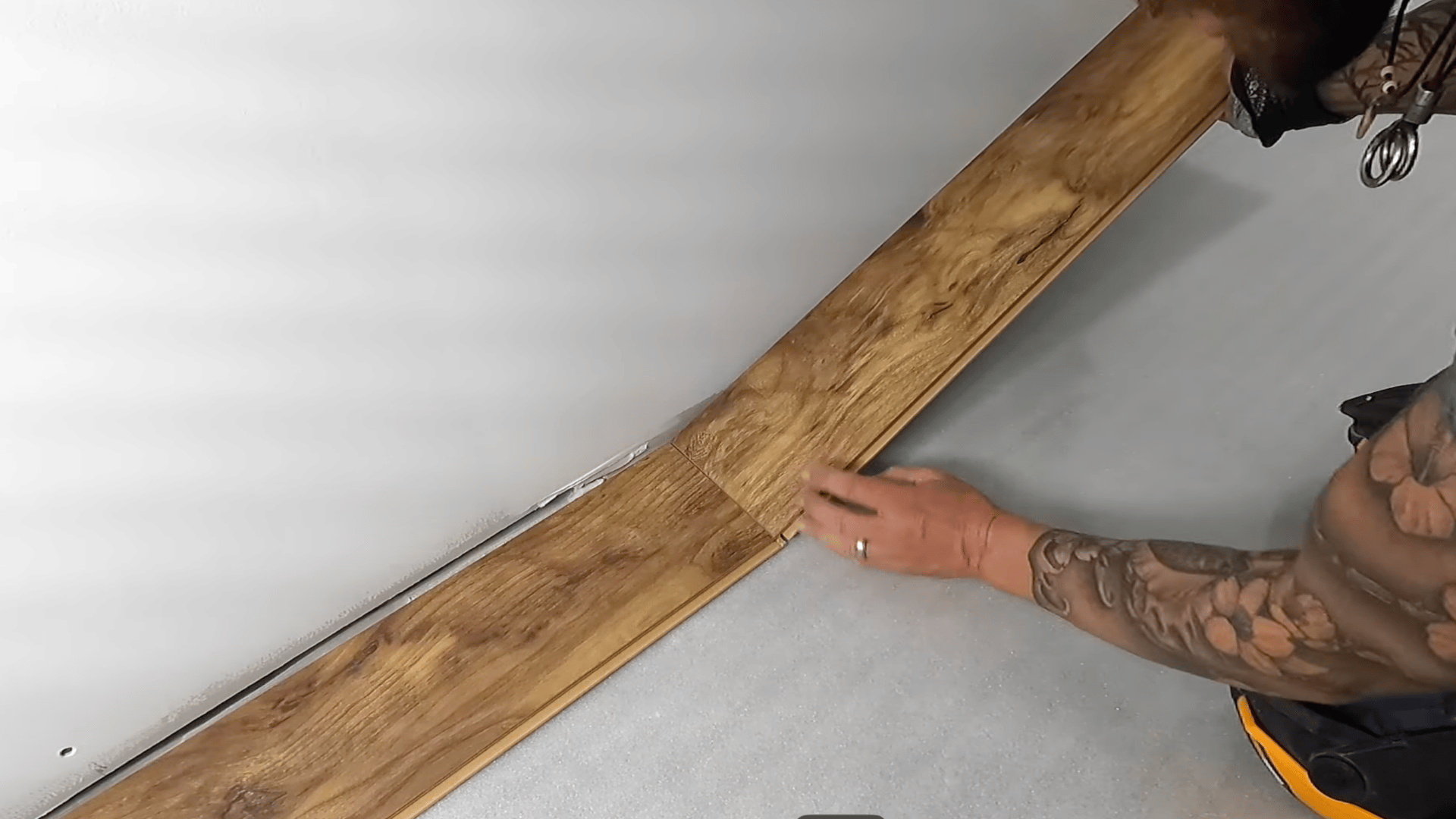 a person is aligning and locking laminate planks together with their hands, ensuring a secure fit along the edge of the wall.