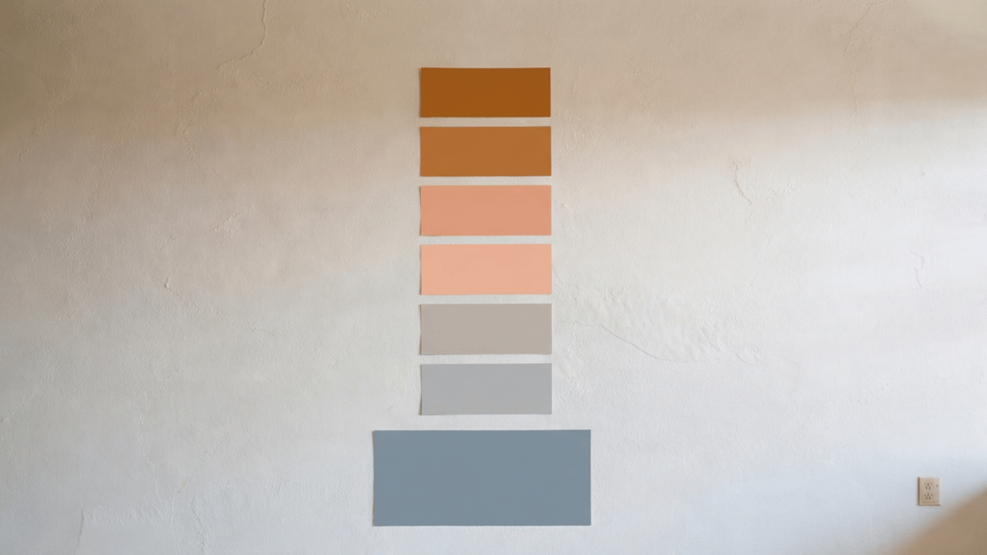 a wall with a series of color swatches in warm terracotta to cool gray arranged in a vertical line for a painting test