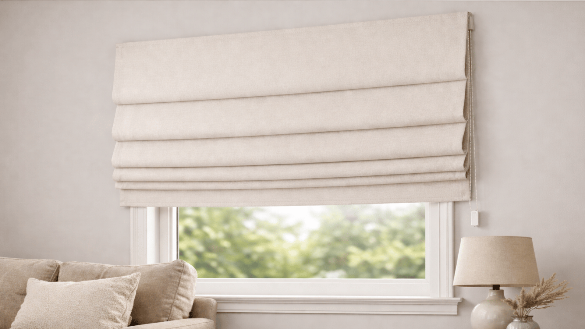 beige roman blind neatly folded above a window with sofa and table lamp in a soft neutral living room setting