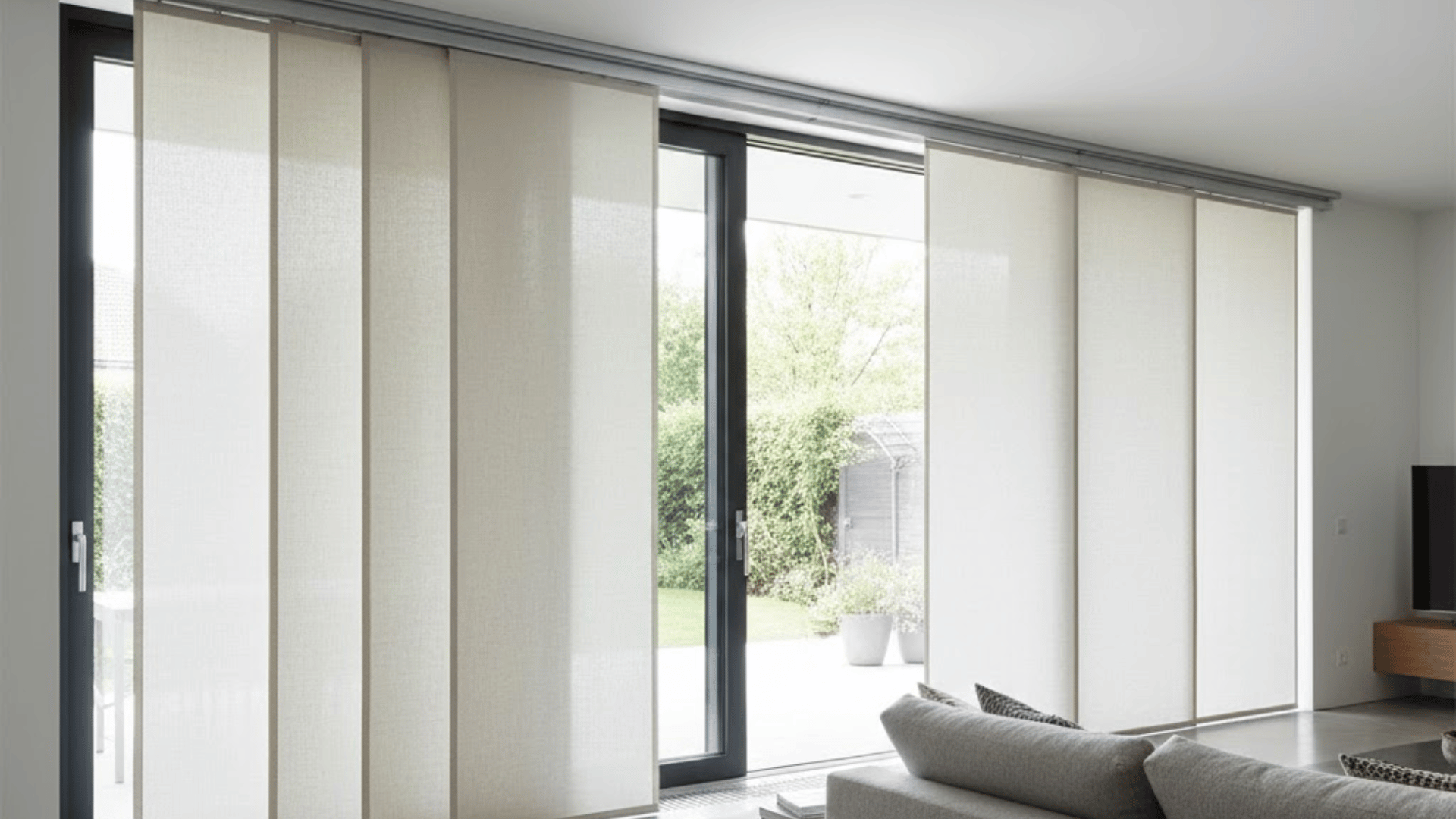elegant beige panel track blinds sliding on a top rail across large glass doors in a minimalist, sunlit living room