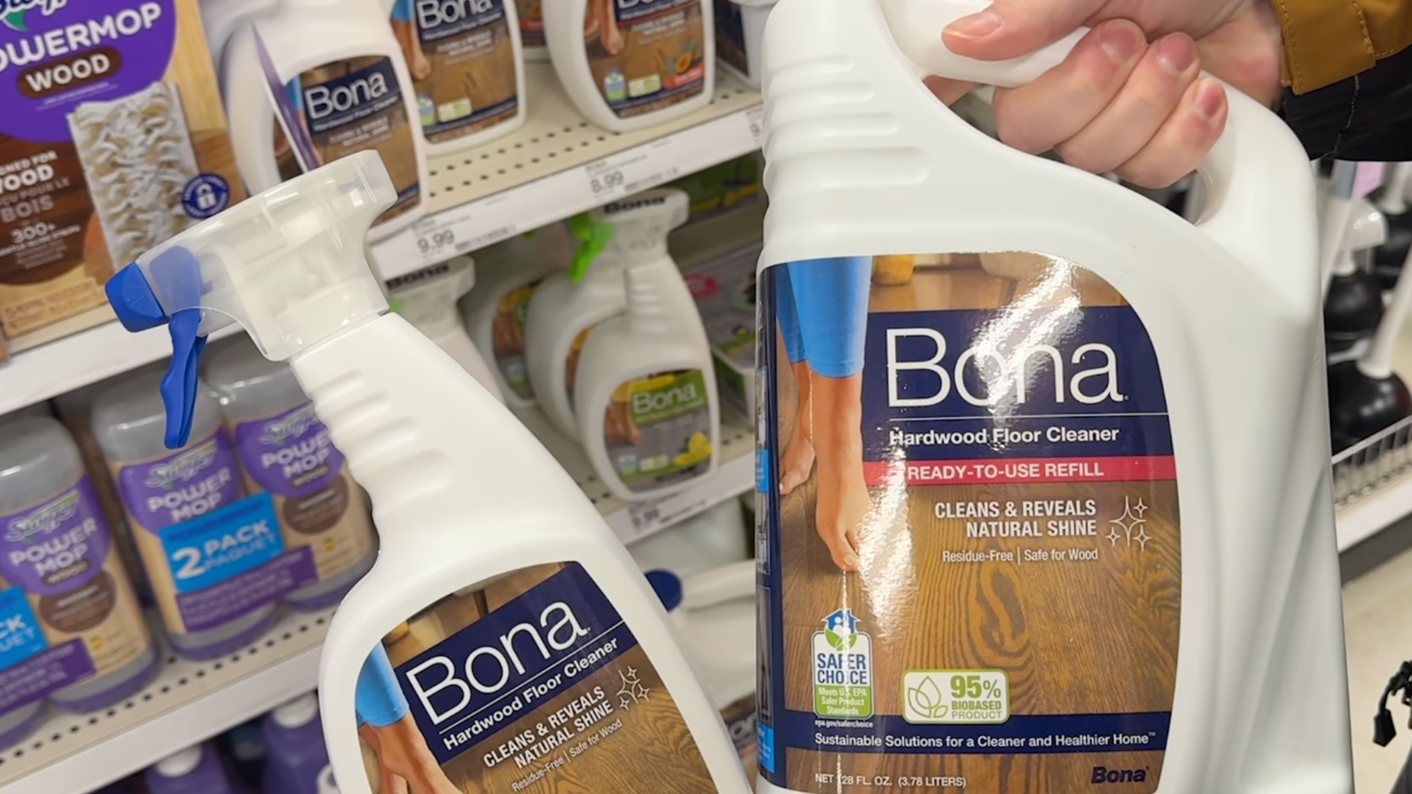 hand holding Bona hardwood floor cleaner spray and refill bottles in a store aisle.