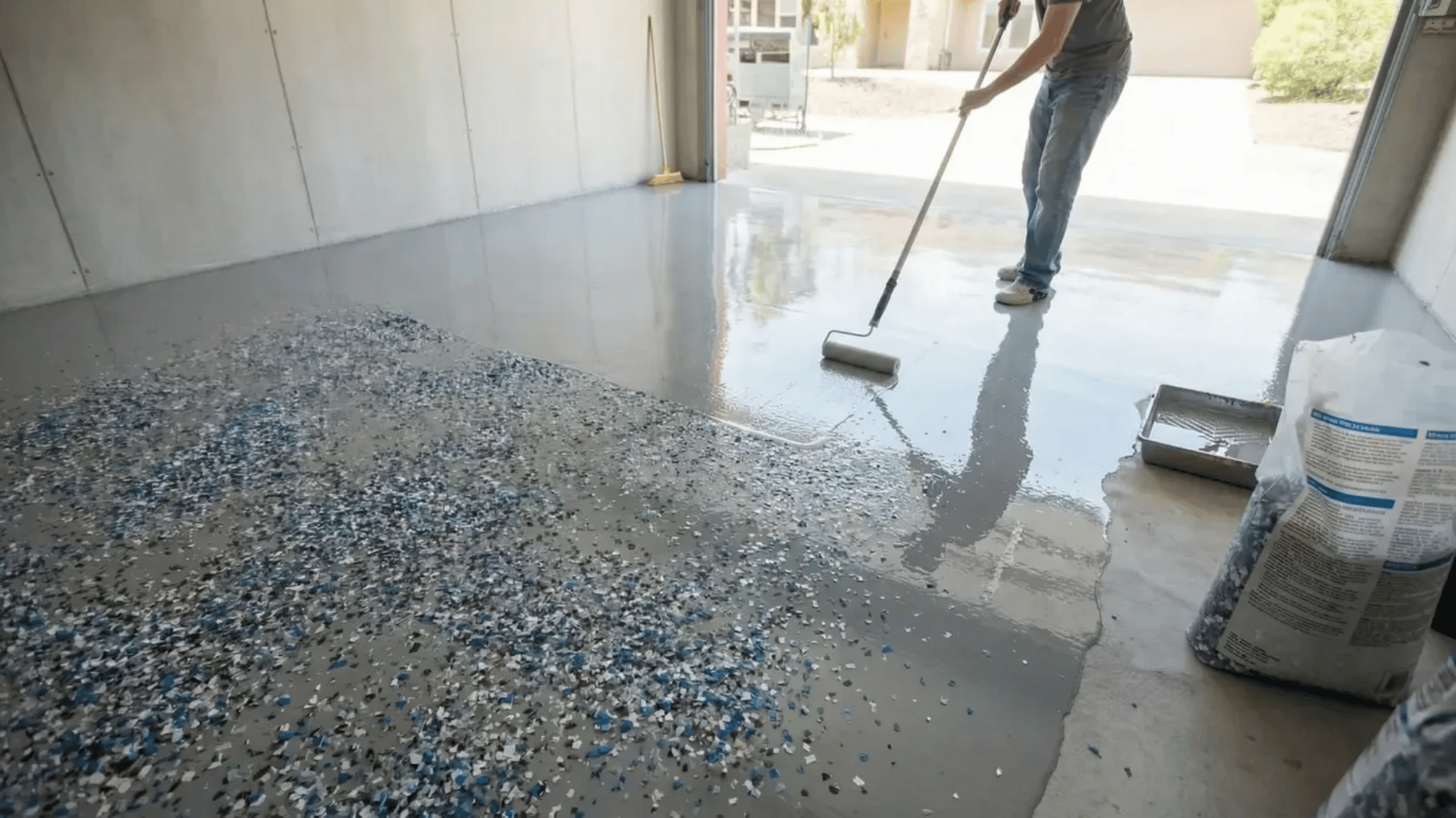 man applying clear topcoat sealer over cured epoxy base layer with roller adding protection and glossy finish to floor