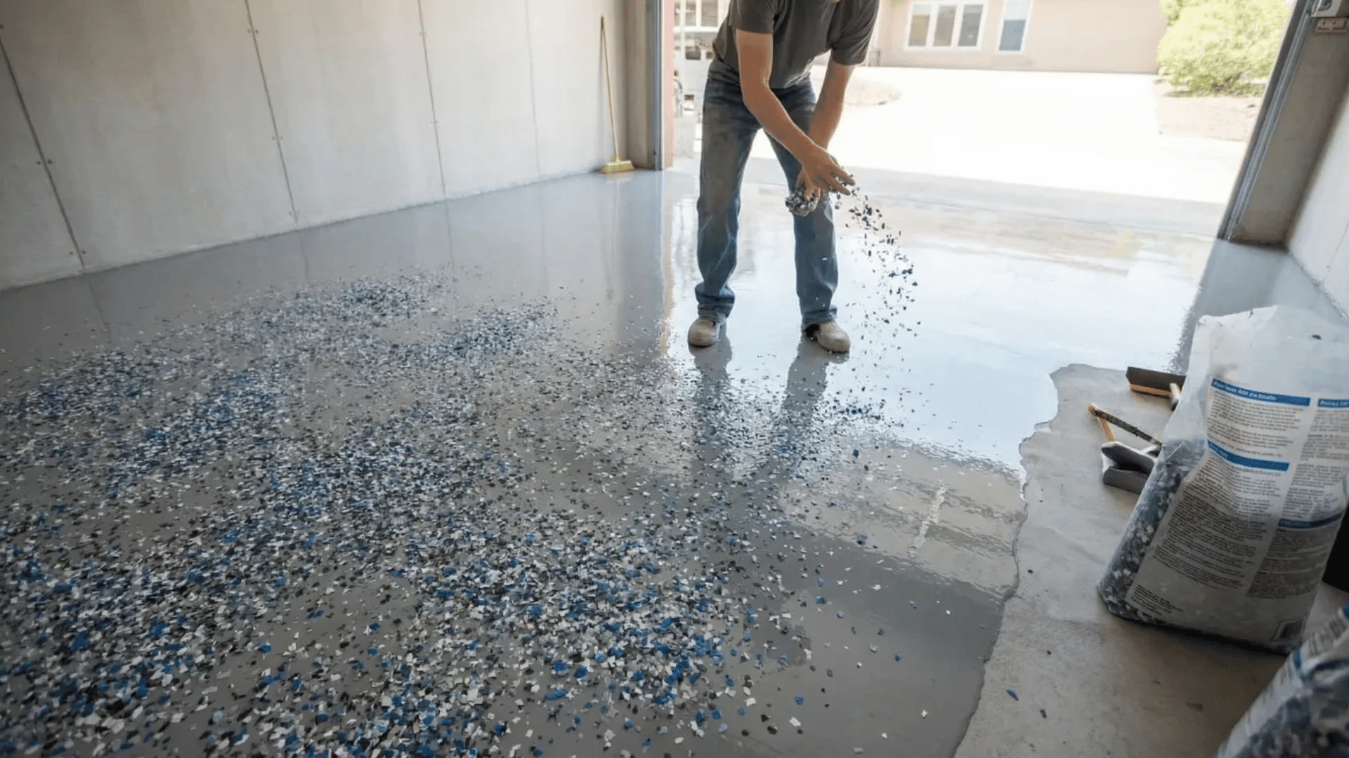 man spreading decorative blue color flakes onto wet epoxy surface by hand creating textured speckled pattern on garage floor