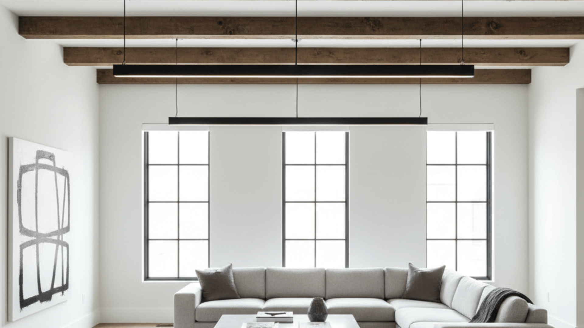 modern living room with rustic wood ceiling beams, sleek linear pendant lights, a gray sectional, and contemporary art.