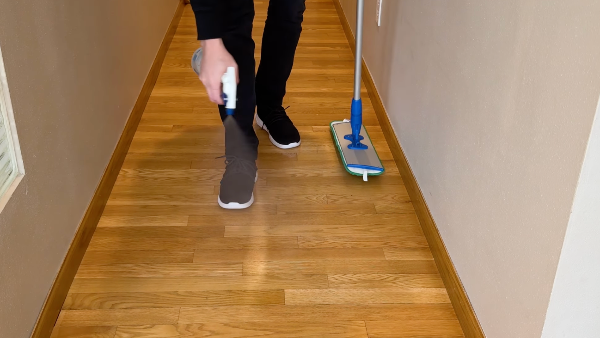 person spraying cleaner on a hardwood floor before mopping in a hallway.