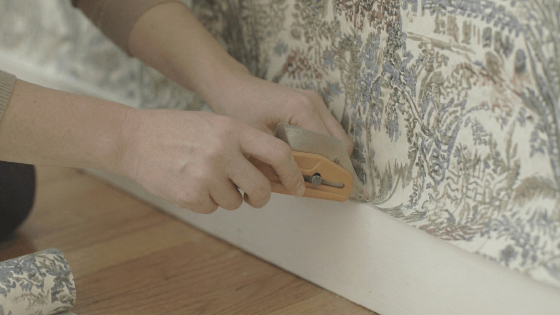 person using a wallpaper seam roller to smooth out the edges of wallpaper along the baseboard