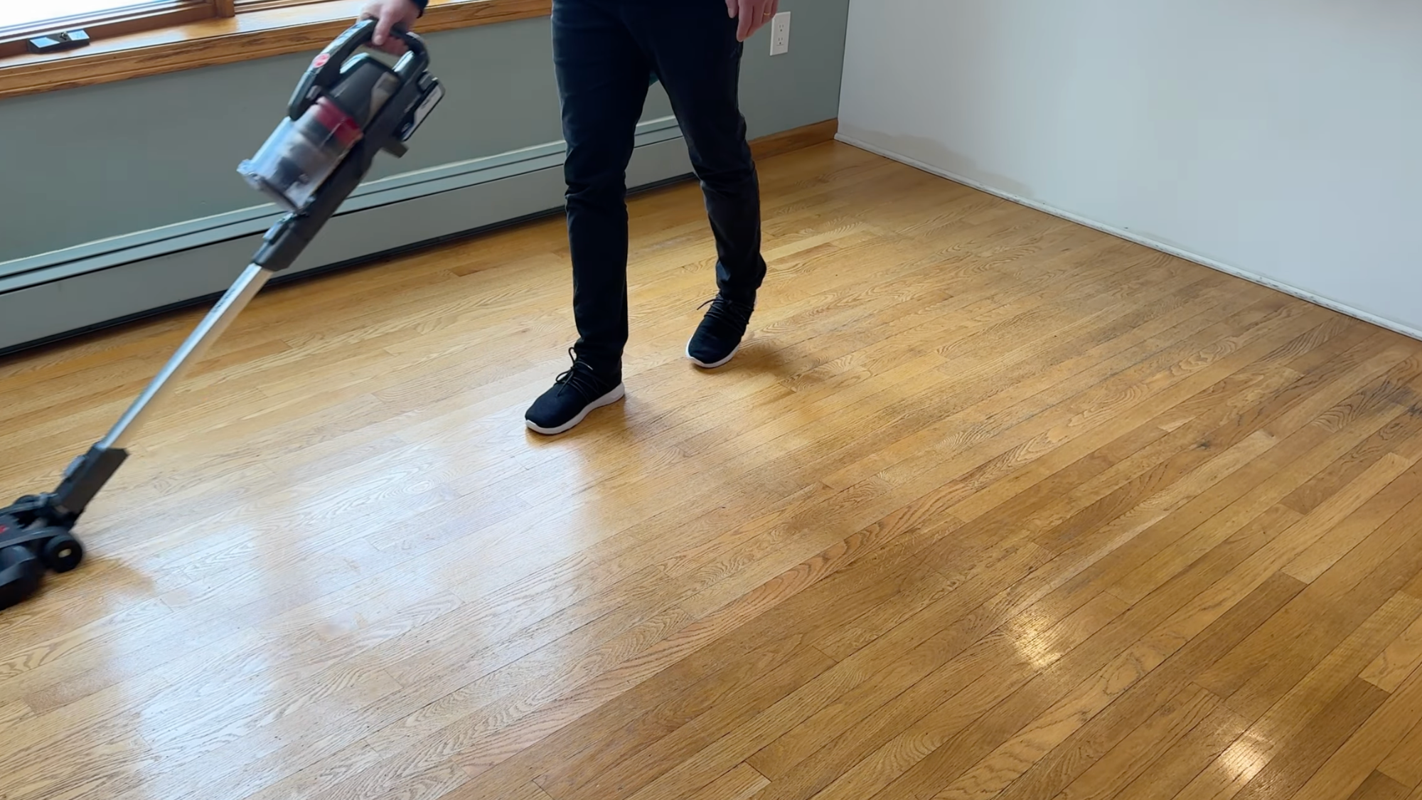 person vacuuming a hardwood floor with a cordless stick vacuum in a bright room. png