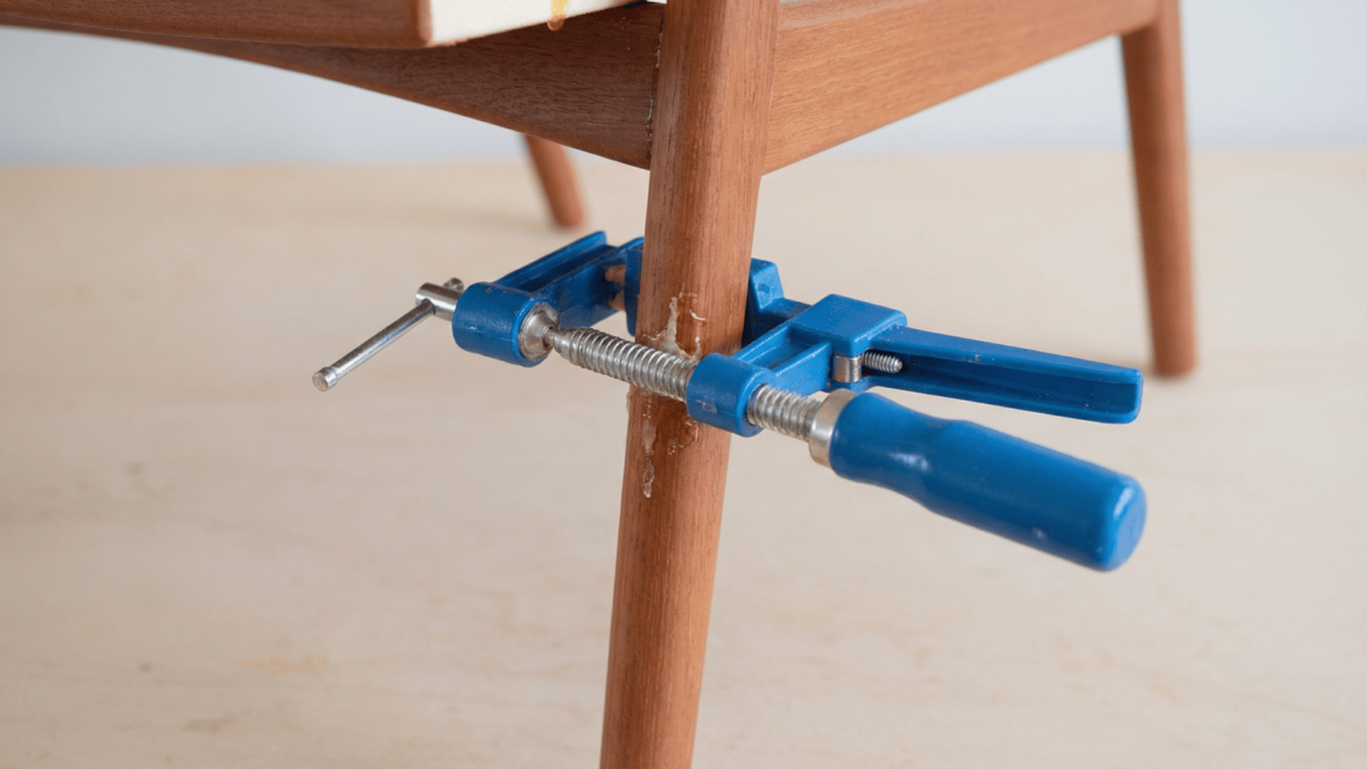reassembled mid-century teak dining chair held together with multiple woodworking clamps at every joint while the epoxy cures
