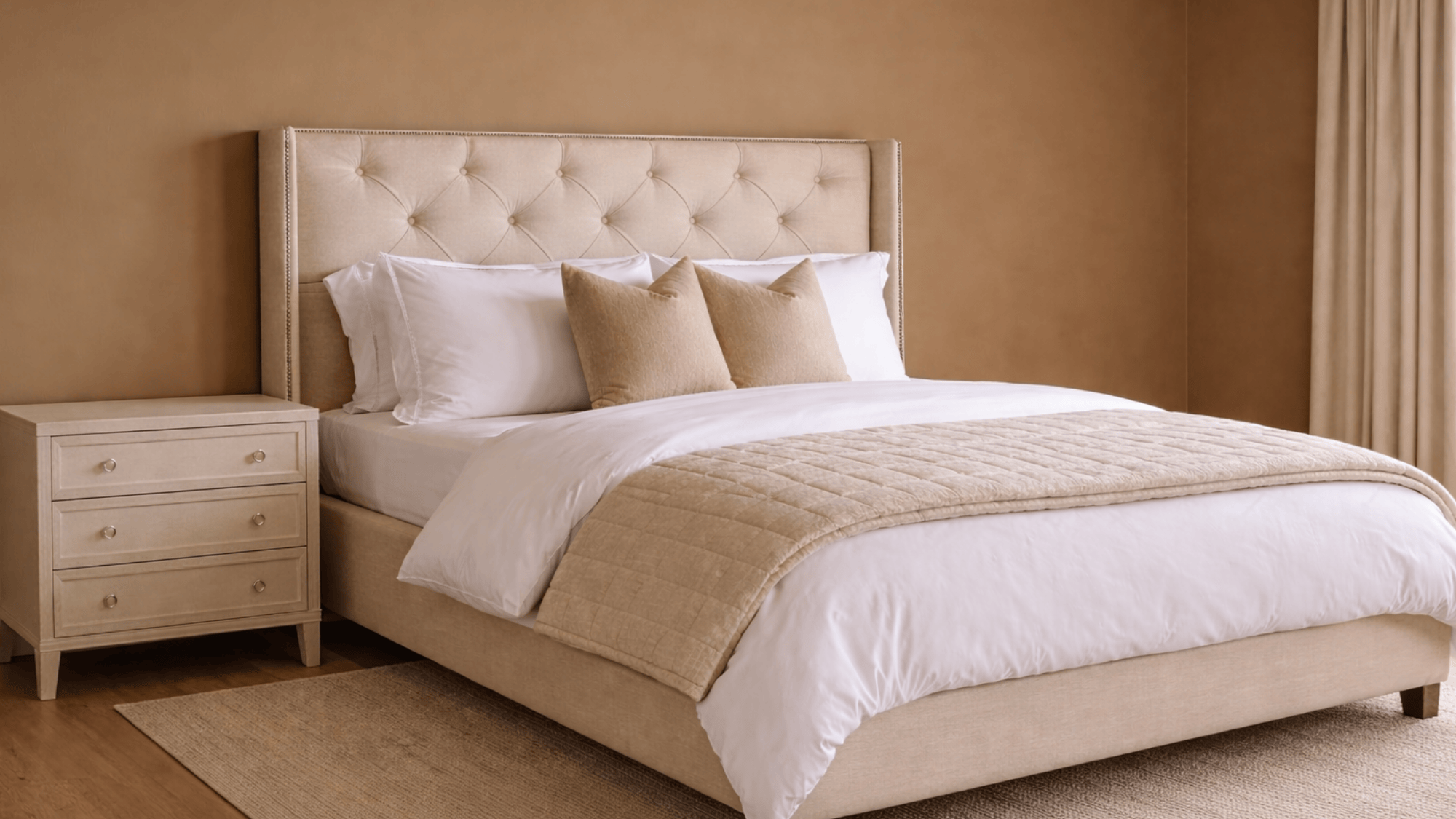side view of a bedroom with a king sized bed, white duvet, patterned and solid pillows, and a beige throw at the foot