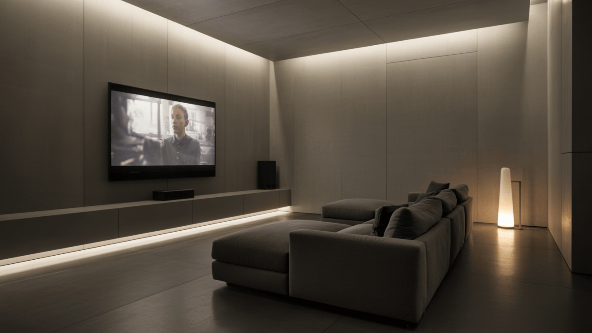 sleek minimalist basement home theater with a wall mounted TV, low lighting, large sectional sofa, and clean modern walls