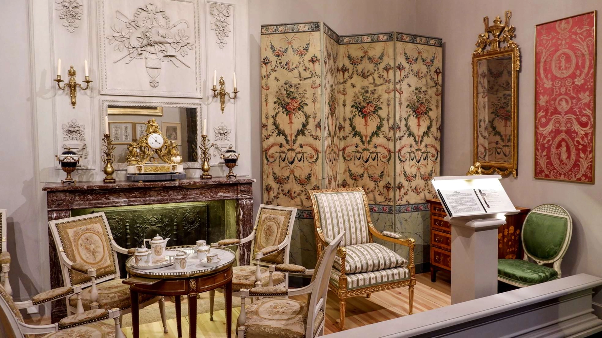 18th-century French Neoclassical room display with gilded chairs, floral folding screen, and marble fireplace
