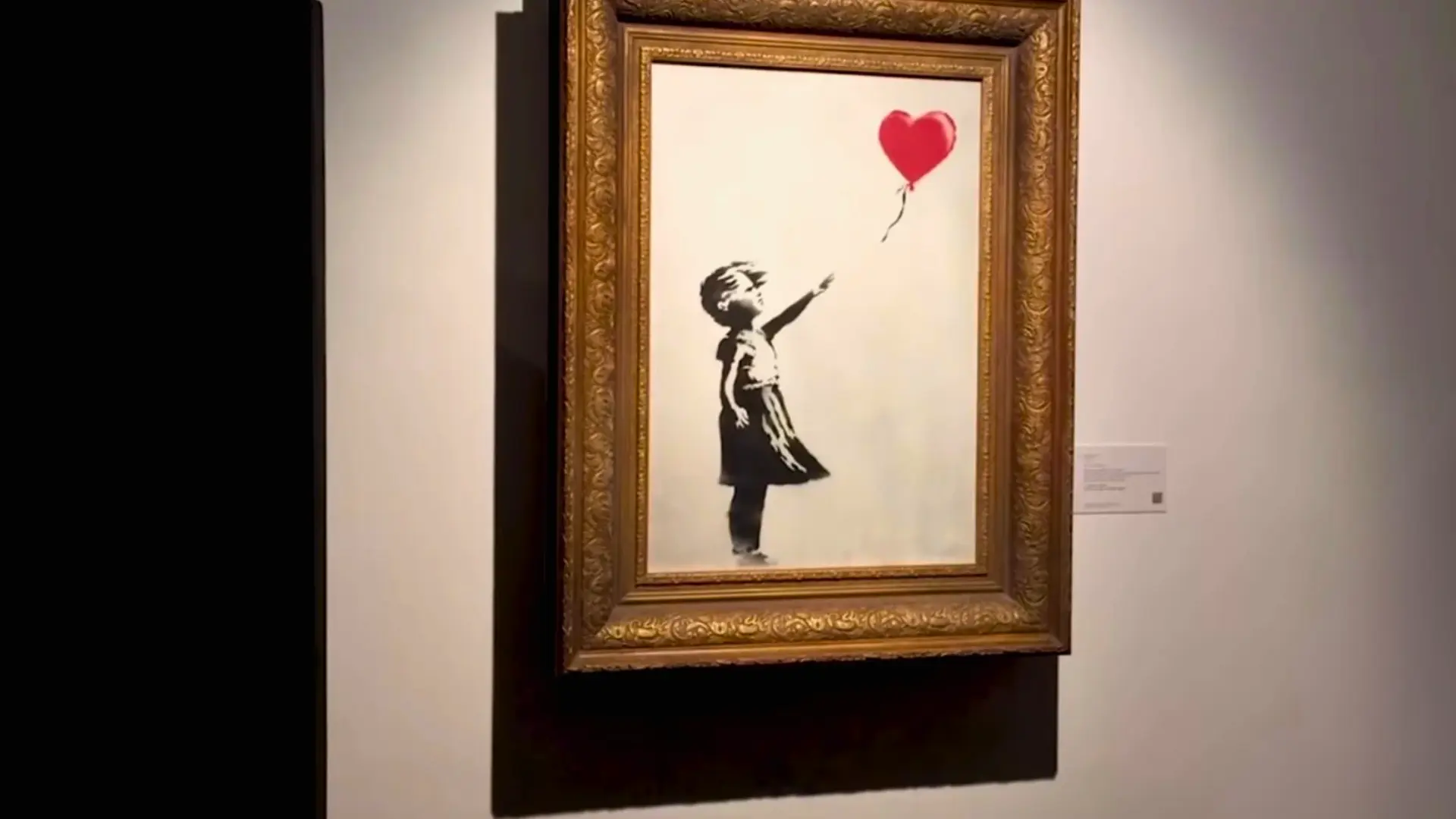 Banksy painting displayed intact in its original frame on a museum wall.