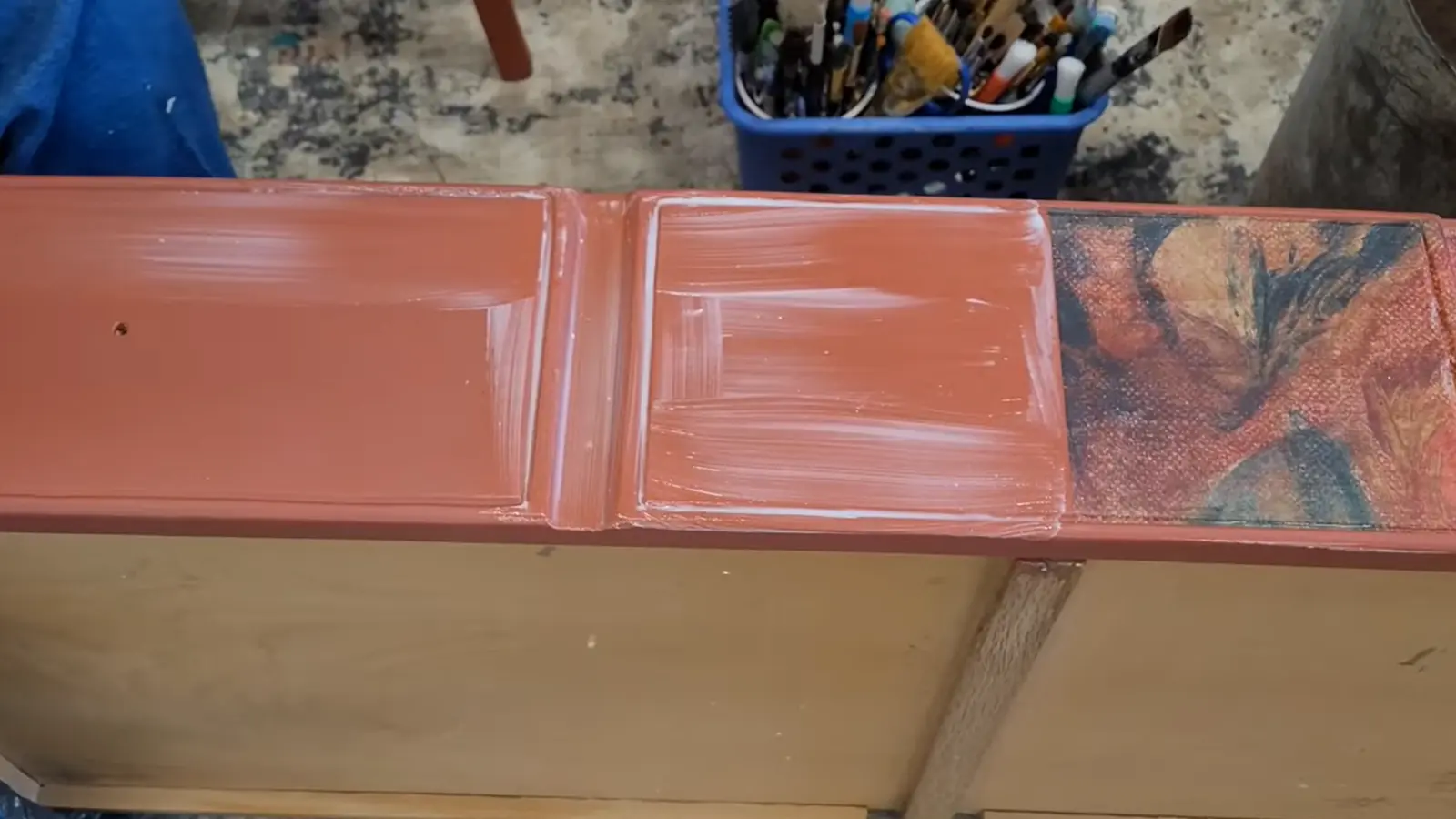 Close-up of dresser drawer front with rust-colored paint being blended along the edge of a floral decoupage section to soften and camouflage the transition.