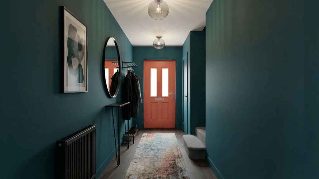 Hallway with teal walls, a round mirror, coat rack with jackets, patterned rug, and a bright orange front door at the end