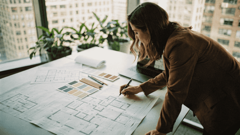 Interior designer reviewing architectural floor plans with color swatches and pencils on a desk near a window