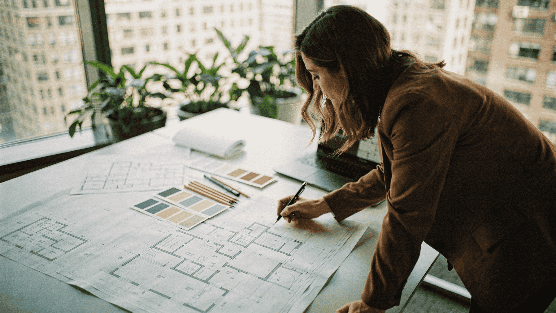 Interior designer reviewing architectural floor plans with color swatches and pencils on a desk near a window