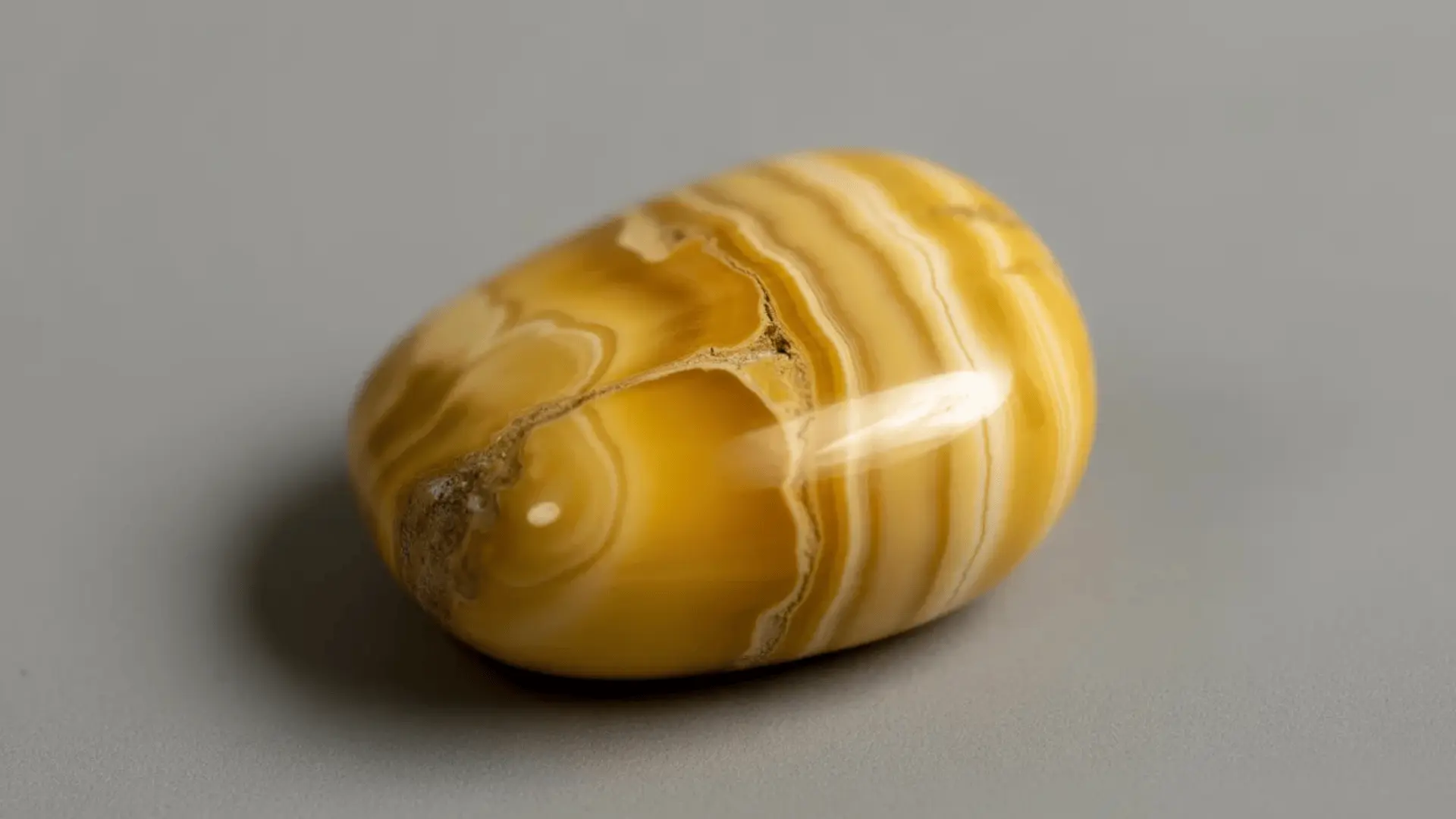 Polished yellow jasper stone with golden to mustard tones and slight natural variations on a neutral background