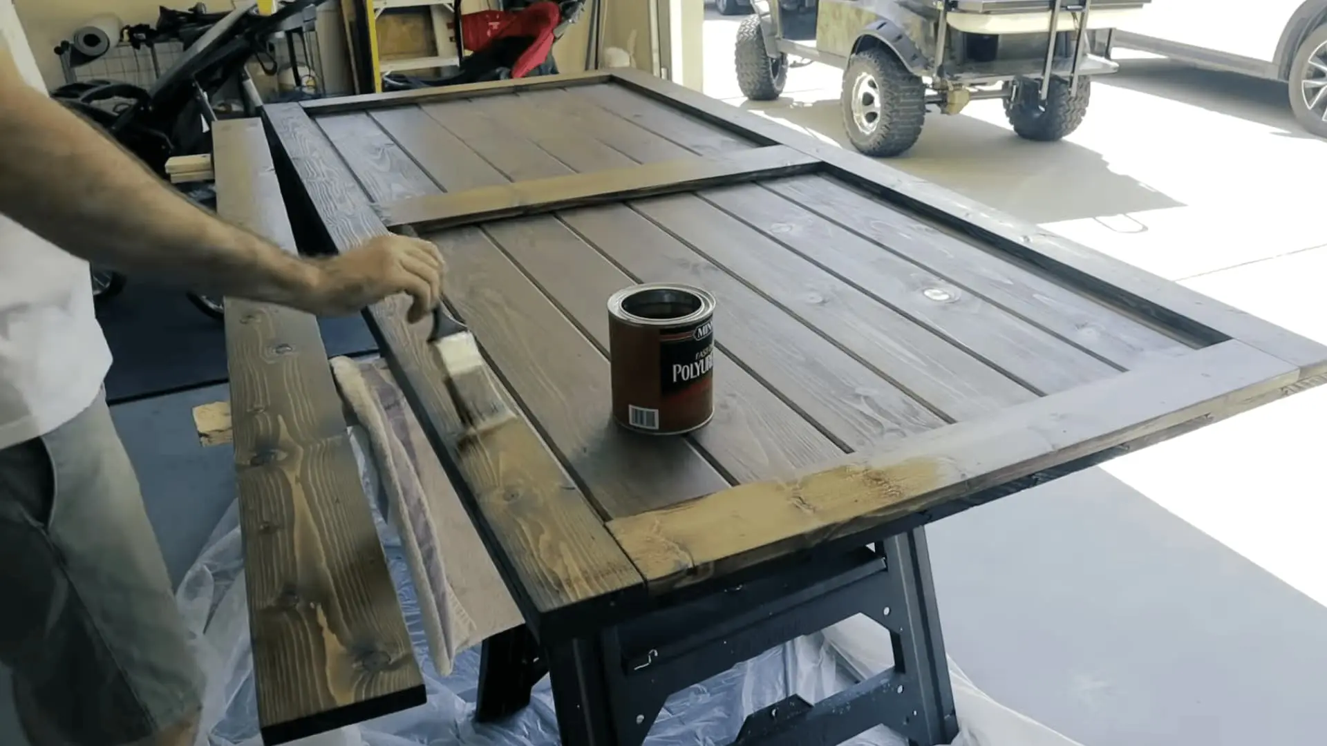 Sanding the assembled barn door and applying wood stain before adding a protective clear coat.