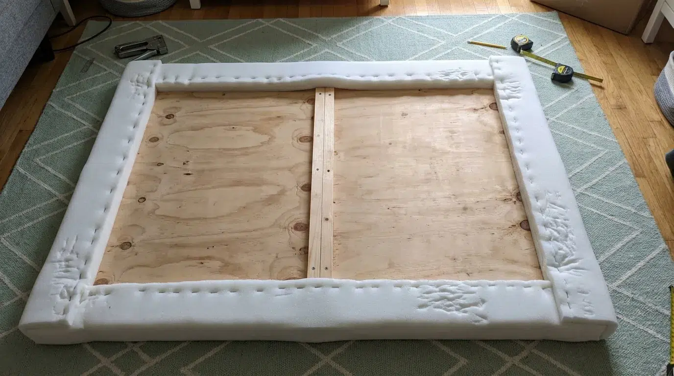 Wrapping white batting around a foam-covered headboard board before stapling it in place