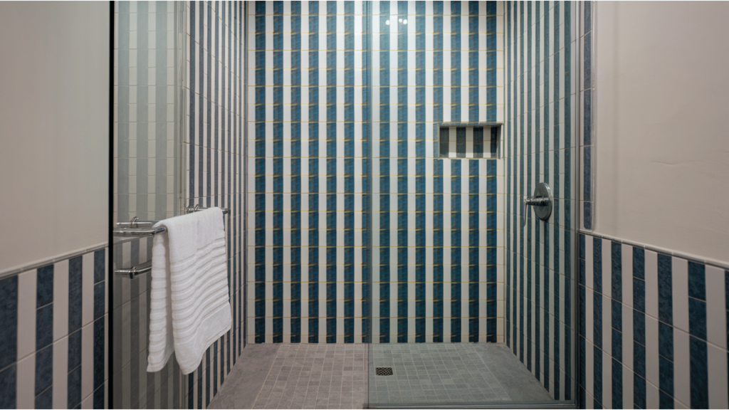 a sleek walk-in shower with vertical striped tiles, a glass partition, and modern chrome fixtures.
