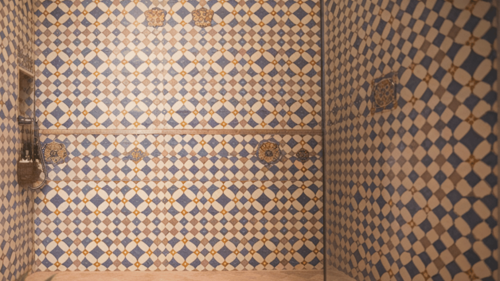 a walk-in shower with blue and yellow patterned tiles, a rainfall showerhead, and a built-in shelf.