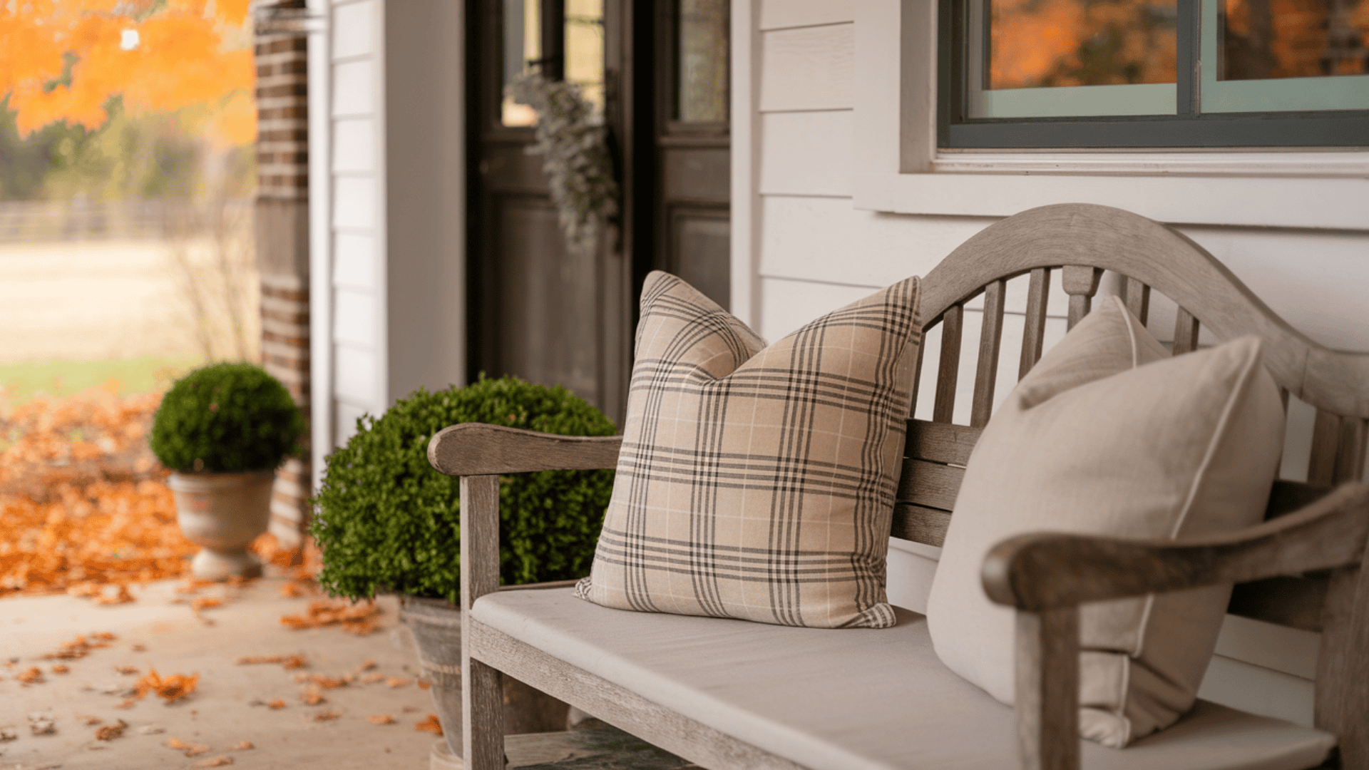 farmhouse porch bench styled with two plaid and neutral tone pillows near the front door in fall