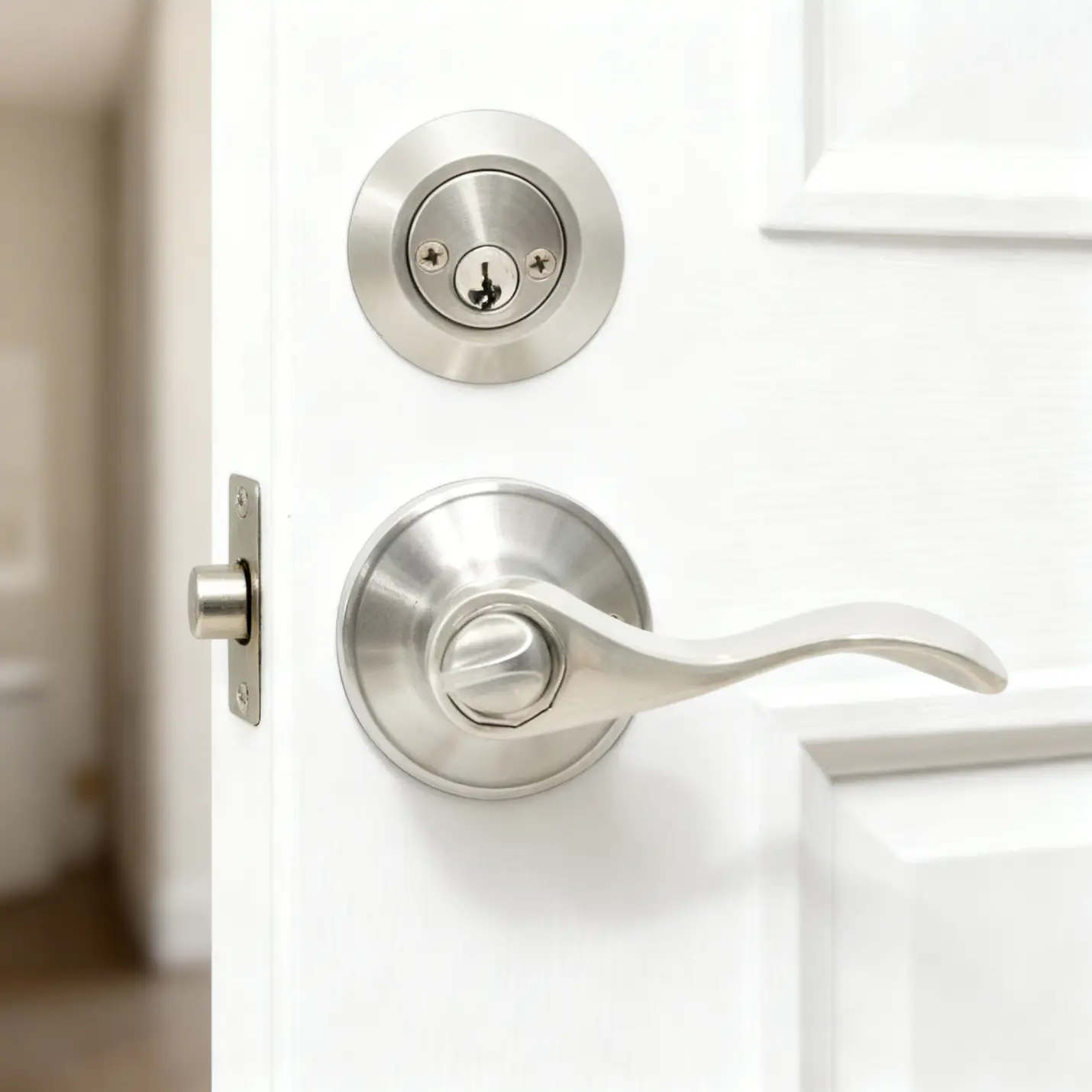Stainless steel door handle and lock on partially open white interior door