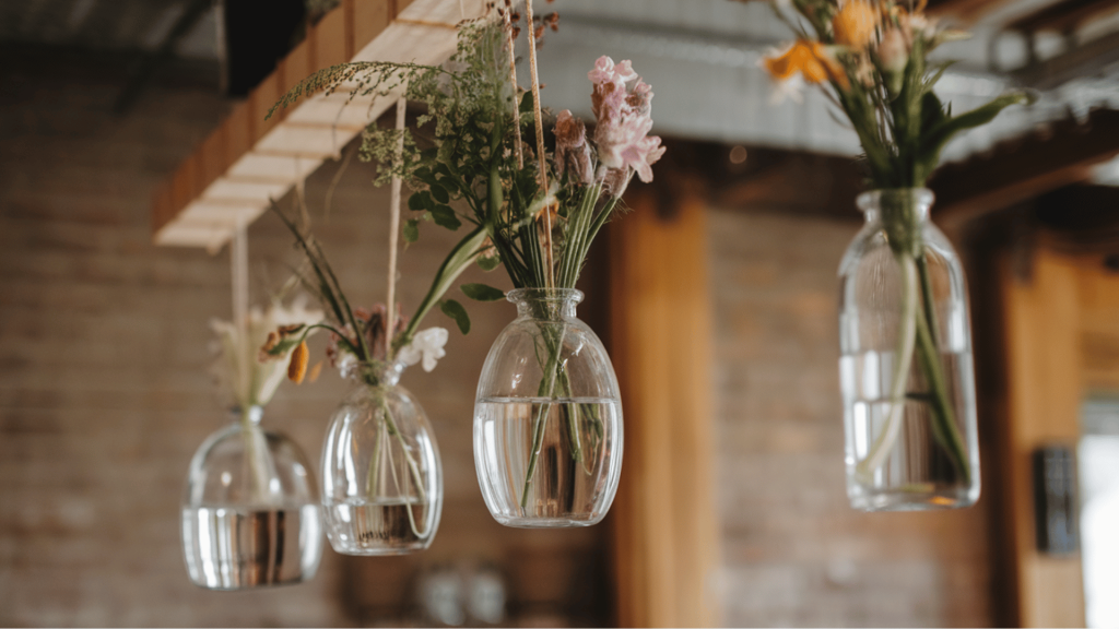 hanging glass vases with wildflowers, suspended from a wooden beam at a rustic wedding.