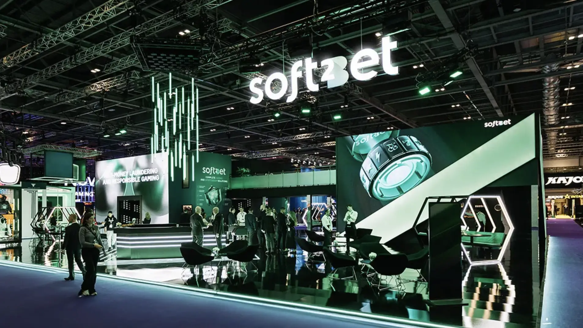 Trade show booth with attendees networking under green lights and large digital display screens