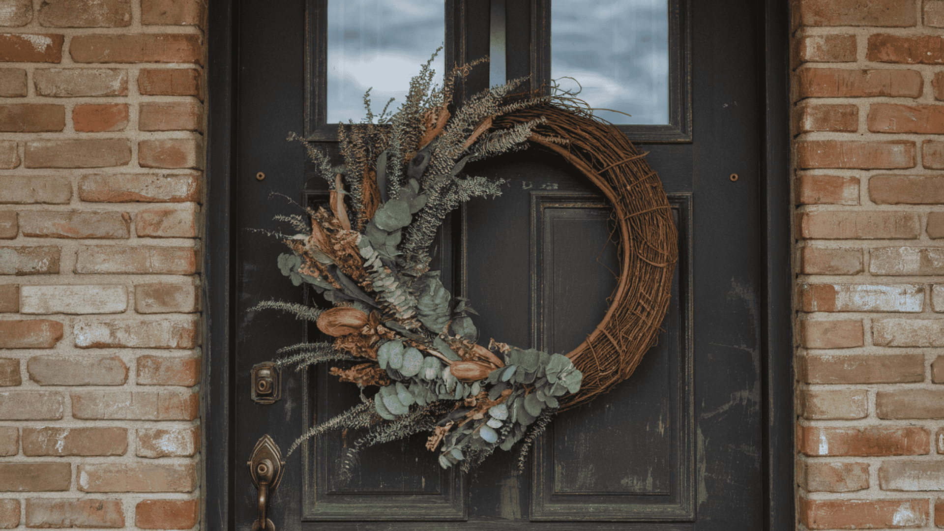 natural grapevine wreath with dried greenery hanging simply on a dark farmhouse front door