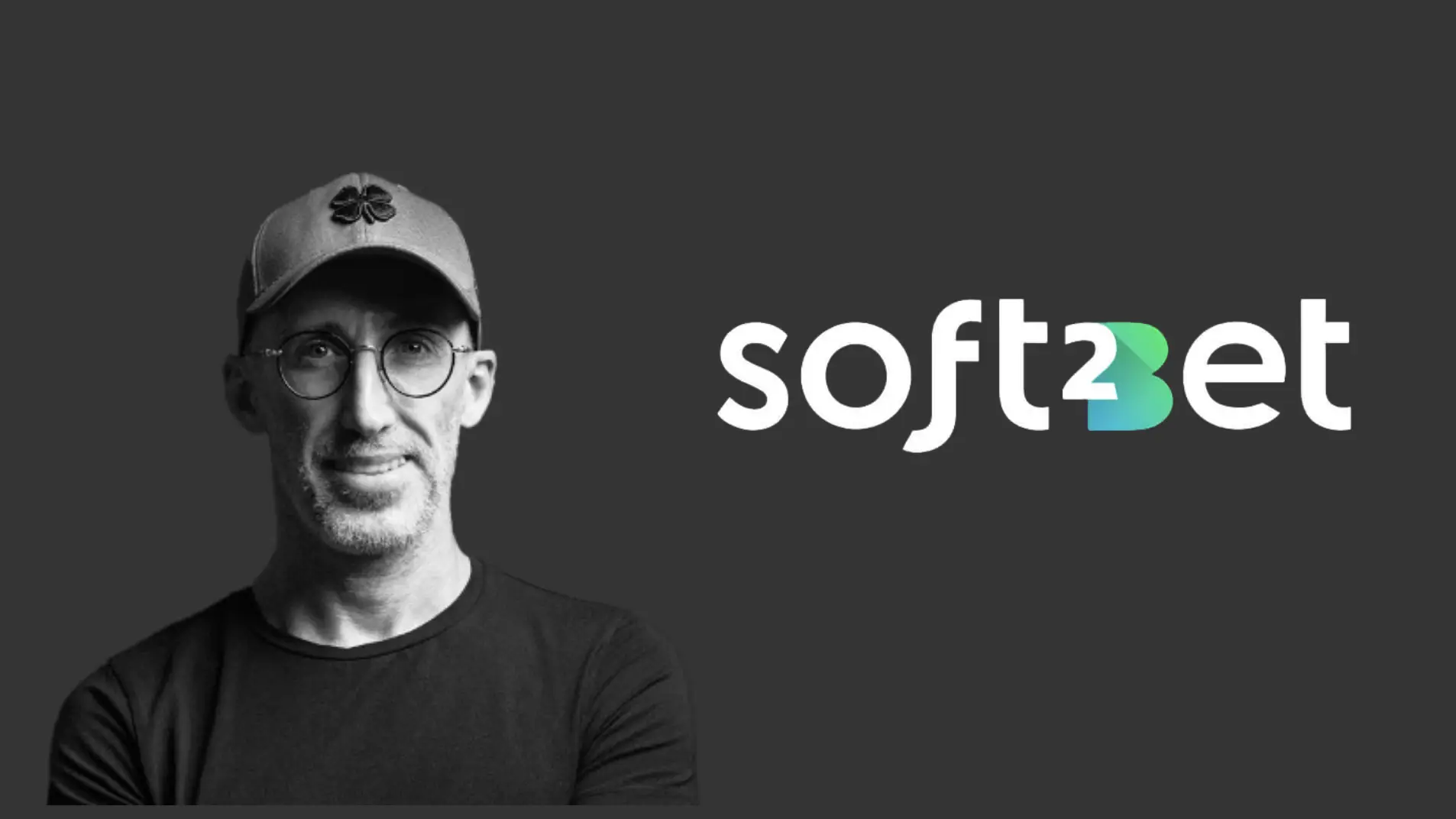 A man in a cap with glasses next to the Soft2Bet logo on a dark background
