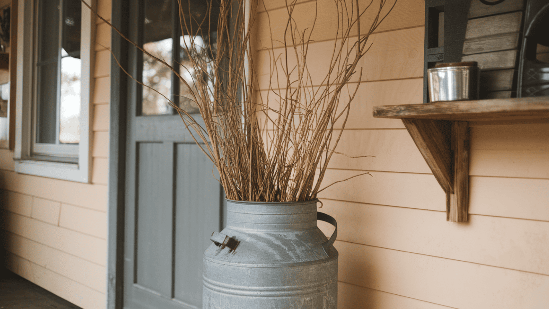 vintage metal milk can filled with tall dried fall branches sitting in a farmhouse porch corner