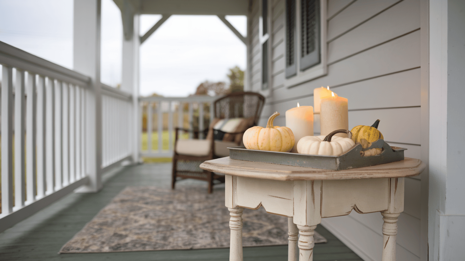 weathered wood side table styled with a tray of mini pumpkins and candles on a fall farmhouse porch