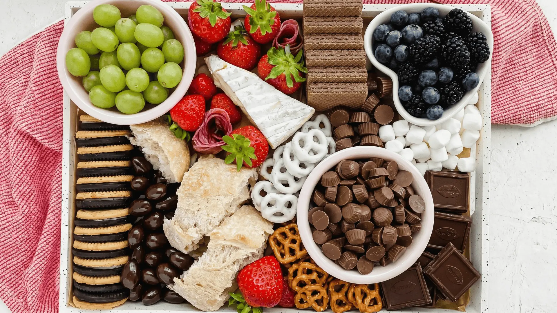 A fruit board with strawberries, apple slices, melted chocolate, dipping sauces, nuts, and light snacks arranged for easy dipping and dessert serving.