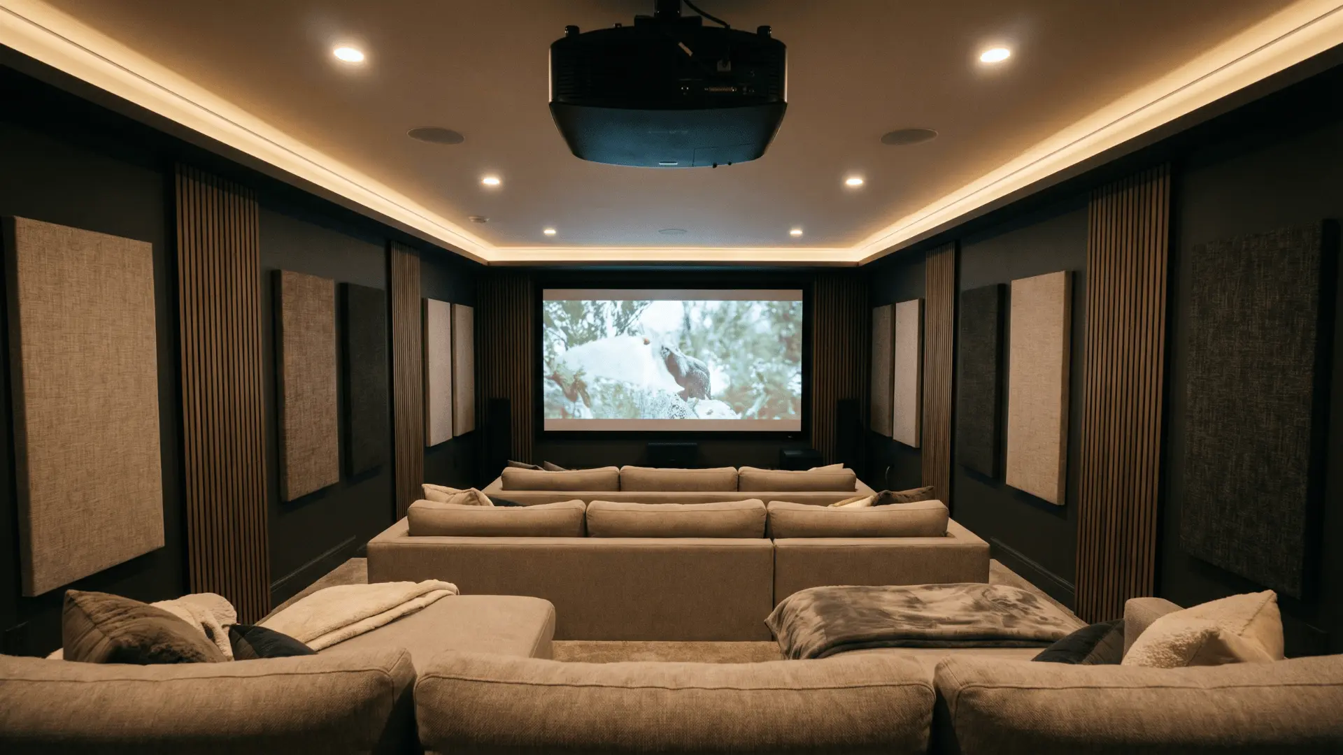 Basement home theater with tiered seating rows, projection screen, acoustic wall panels, and dimmable overhead lighting