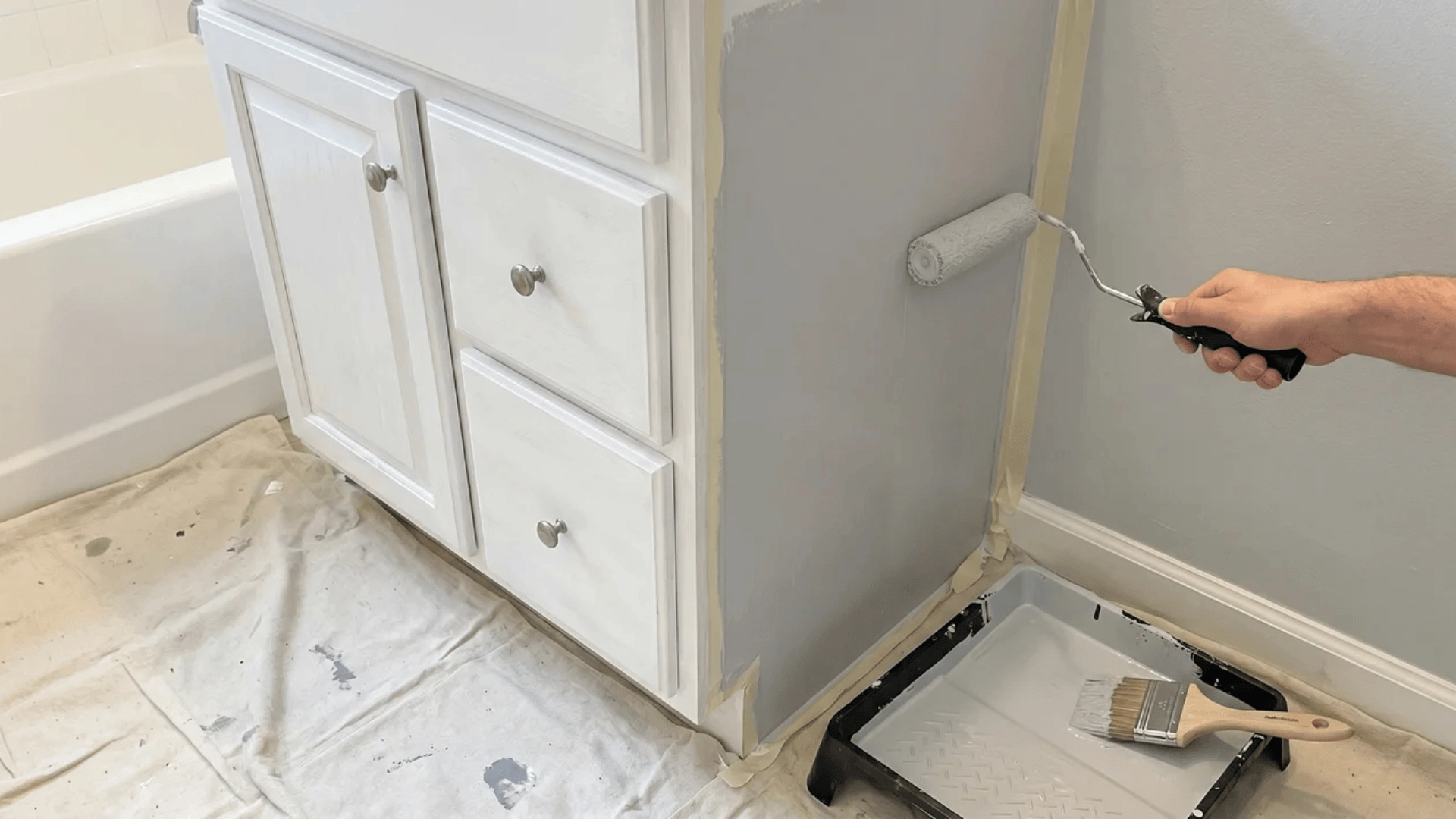 Bathroom wall and cabinet being painted with roller and brush