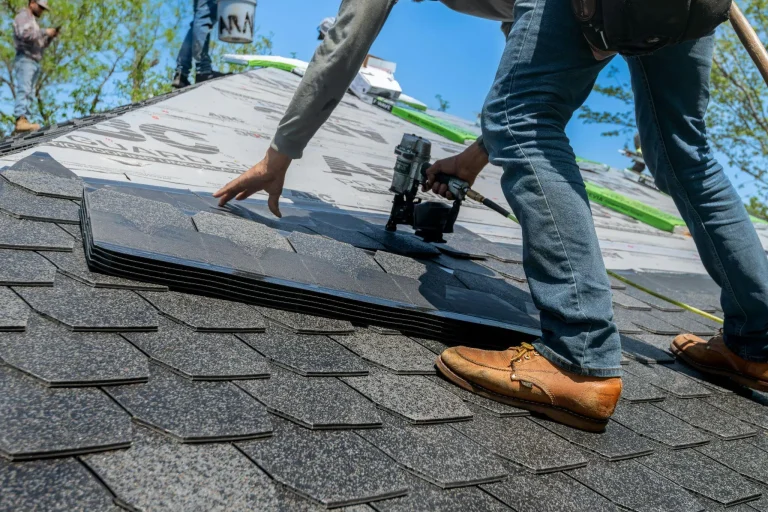 Roofing contractor installing shingles with nail gun under blue sky