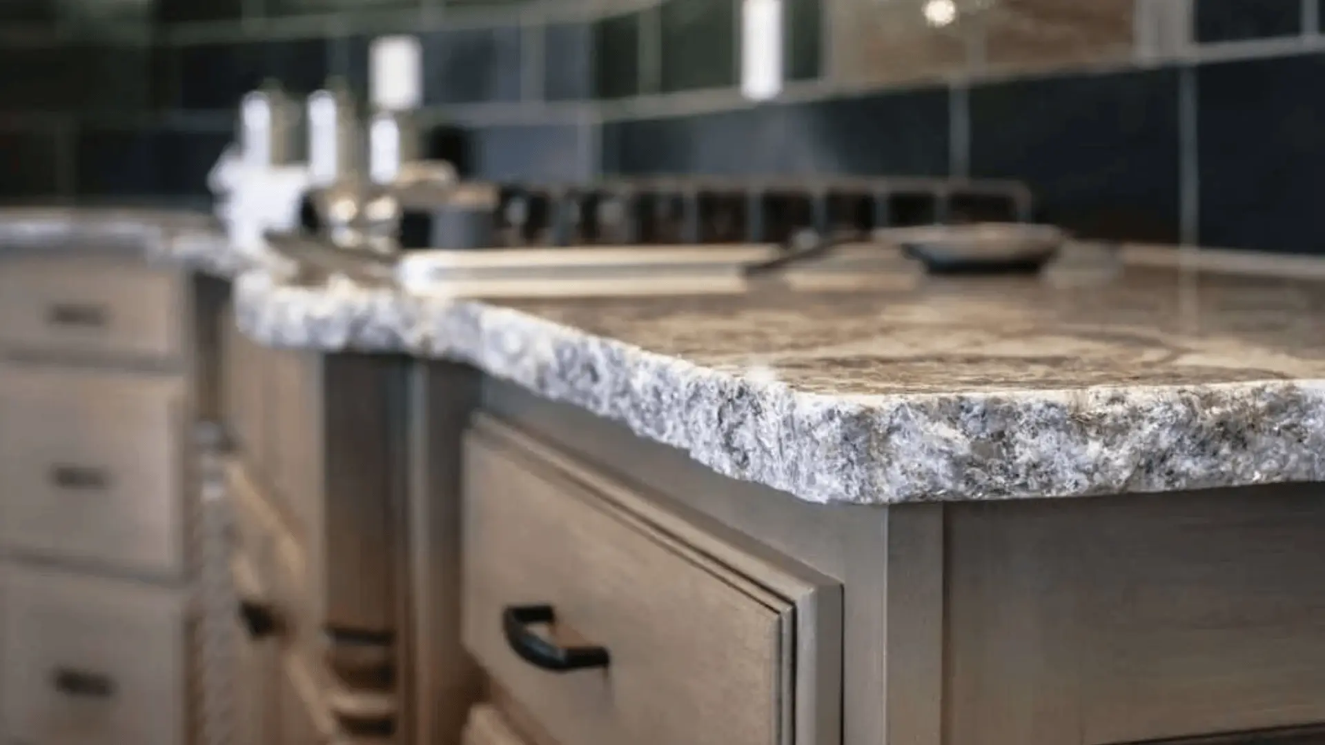 Close-up of a white and gray granite countertop with blue veining and rough edges over gray cabinets