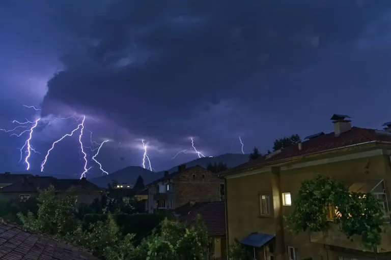 Lightning strikes illuminating a stormy night sky over houses and trees