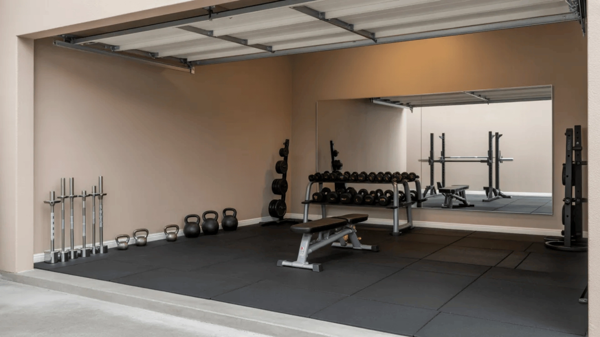 Garage converted into gym with weights, rubber flooring, and mirror