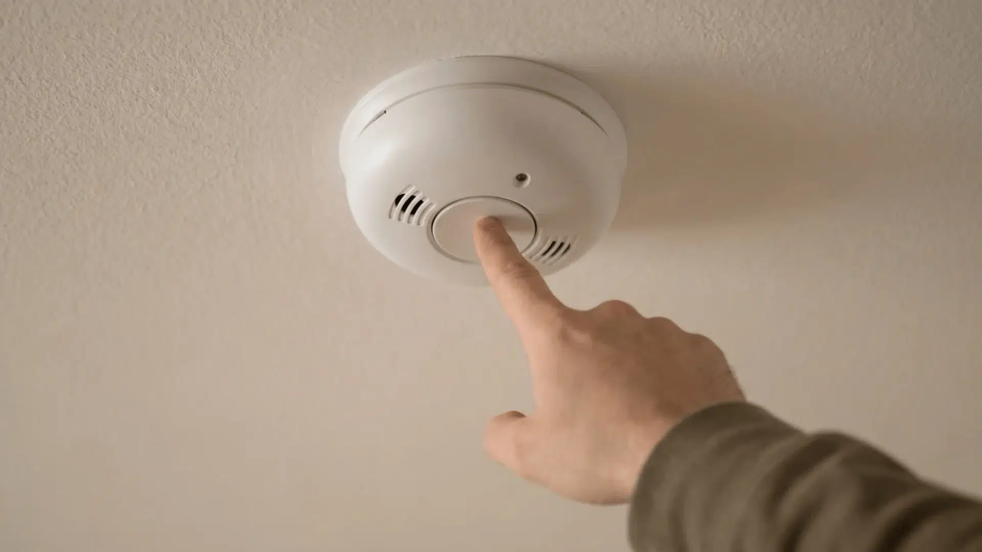 Hand pressing test button on ceiling smoke detector