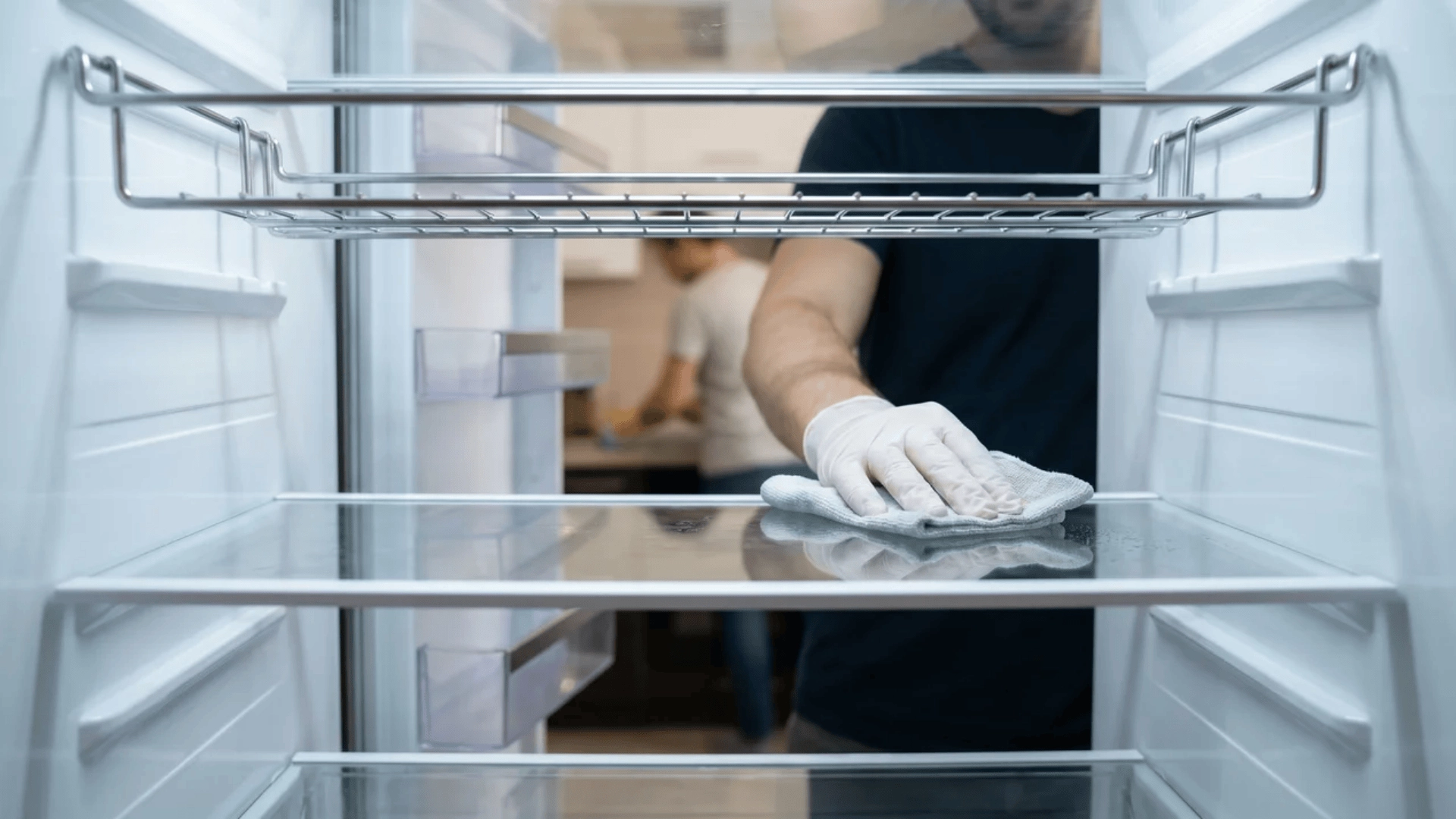 Hand wiping inside shelf of empty refrigerator
