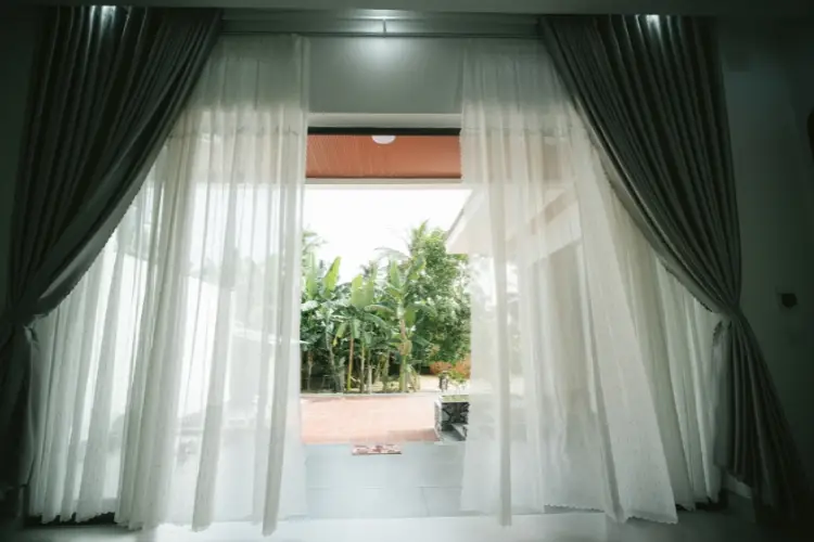 Sheer white curtains framing open doorway with garden view in bright living room